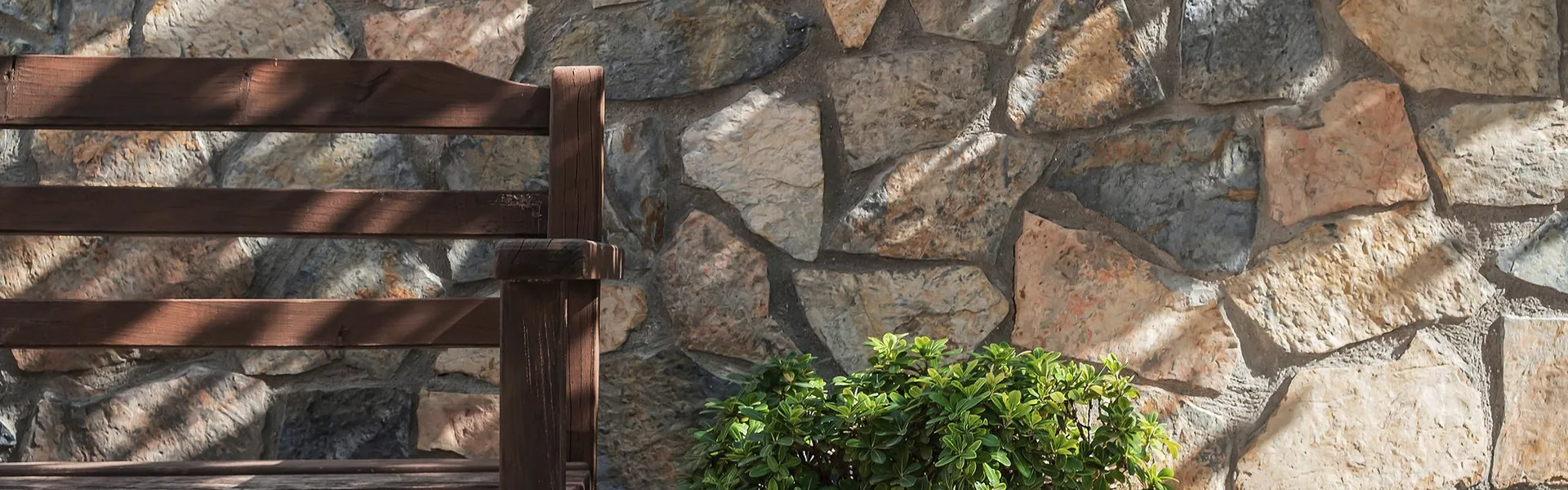pared de piedra con banco de madera y planta