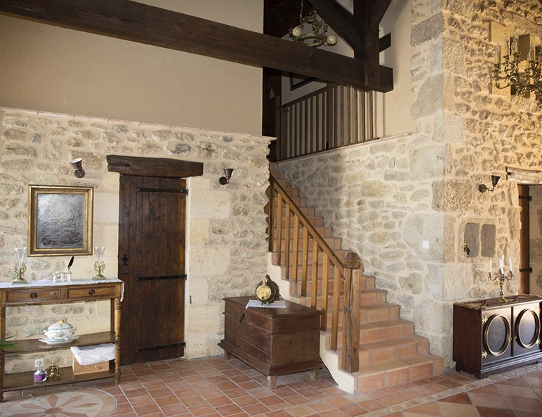 Interior de casa rural con paredes de piedra y escalera y vigas techo de madera